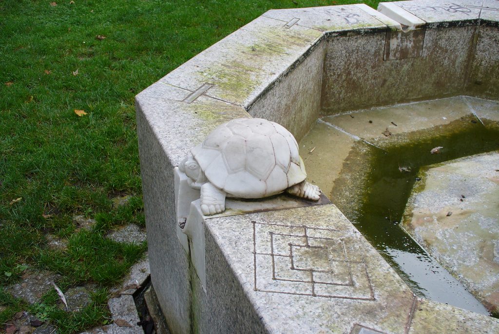 Die Landschildkröte aus Marmor sitzt direkt auf dem Rand des achteckigen Brunnenbeckens.
